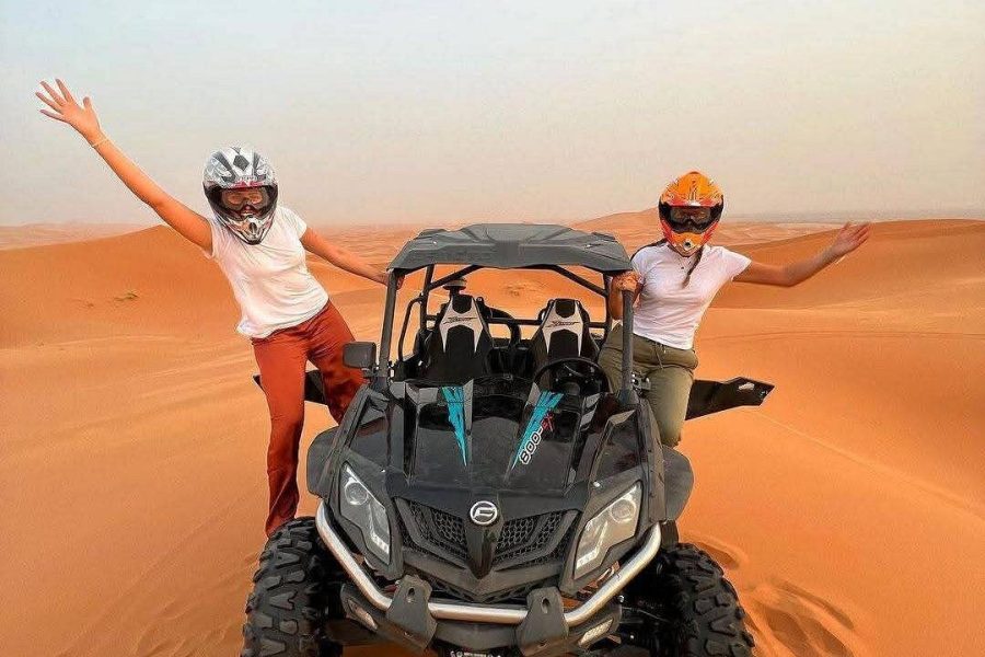 Traveler riding a quad bike across golden dunes near Tamri, with the Atlantic Ocean in the background and dust rising behind.